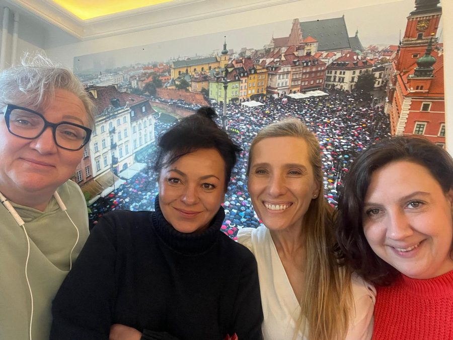 Four women in the Strajk Kobiet office, photographed in front of a wall-sized image of the Warsaw protests